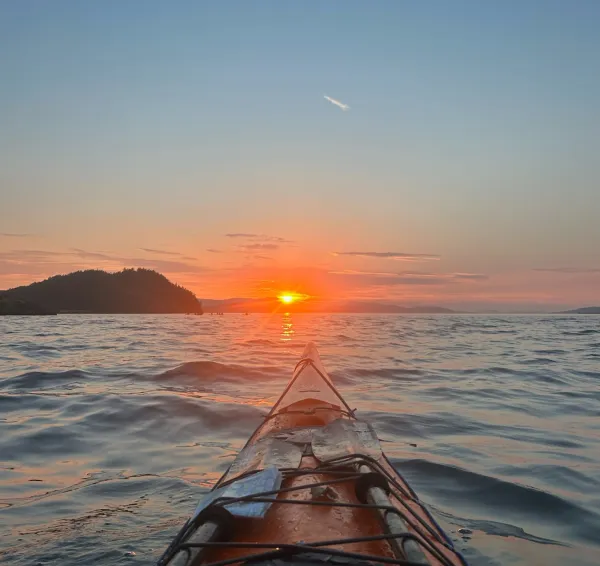 Tip of a kayak with the sunset on the horizon